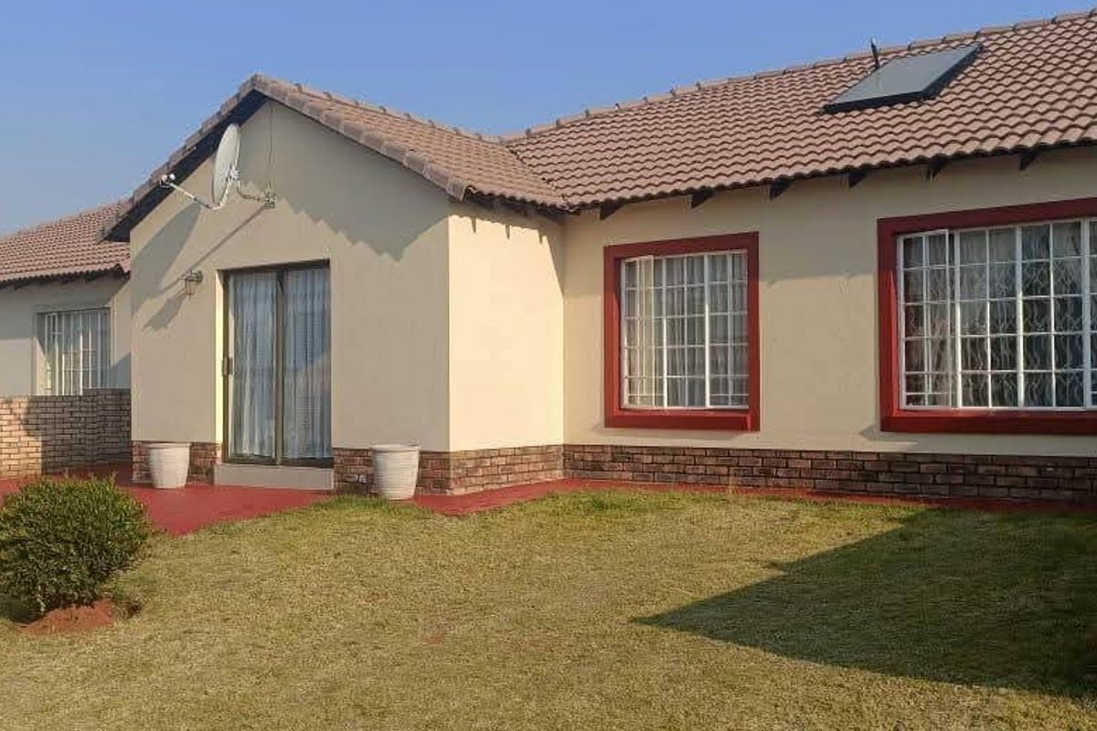 Rear view of the house featuring a tiled roof, brick boundary walls, a sliding glass door, and a small lawn area.