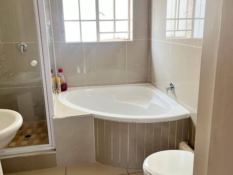 A functional bathroom featuring a corner bathtub, separate shower enclosure, pedestal basin, and toilet with neutral wall and floor tiling.