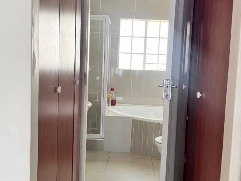 A hallway featuring built-in wooden cupboards and tiled flooring, providing direct access to an adjoining bathroom.