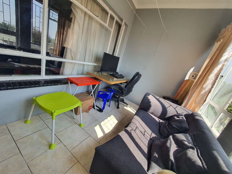 A sunlit enclosed balcony or patio area featuring tiled flooring and large windows, suitable for use as a home office or relaxation space.