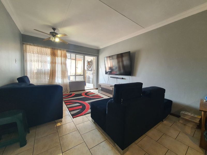 A comfortable living room featuring tiled flooring, a ceiling fan, and direct access to an adjoining patio area through a sliding glass door.