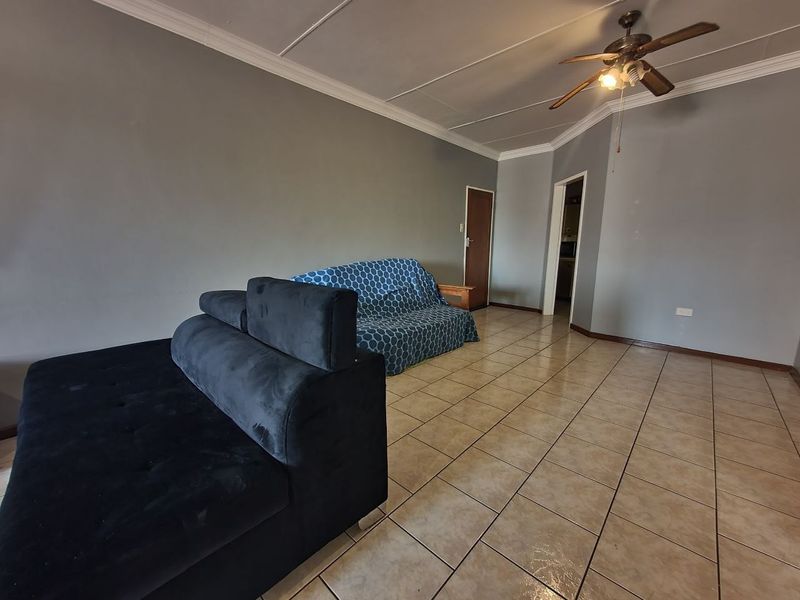 A living room featuring tiled flooring, a ceiling fan, and coved cornicing, requiring some cosmetic updates to the walls and ceiling.