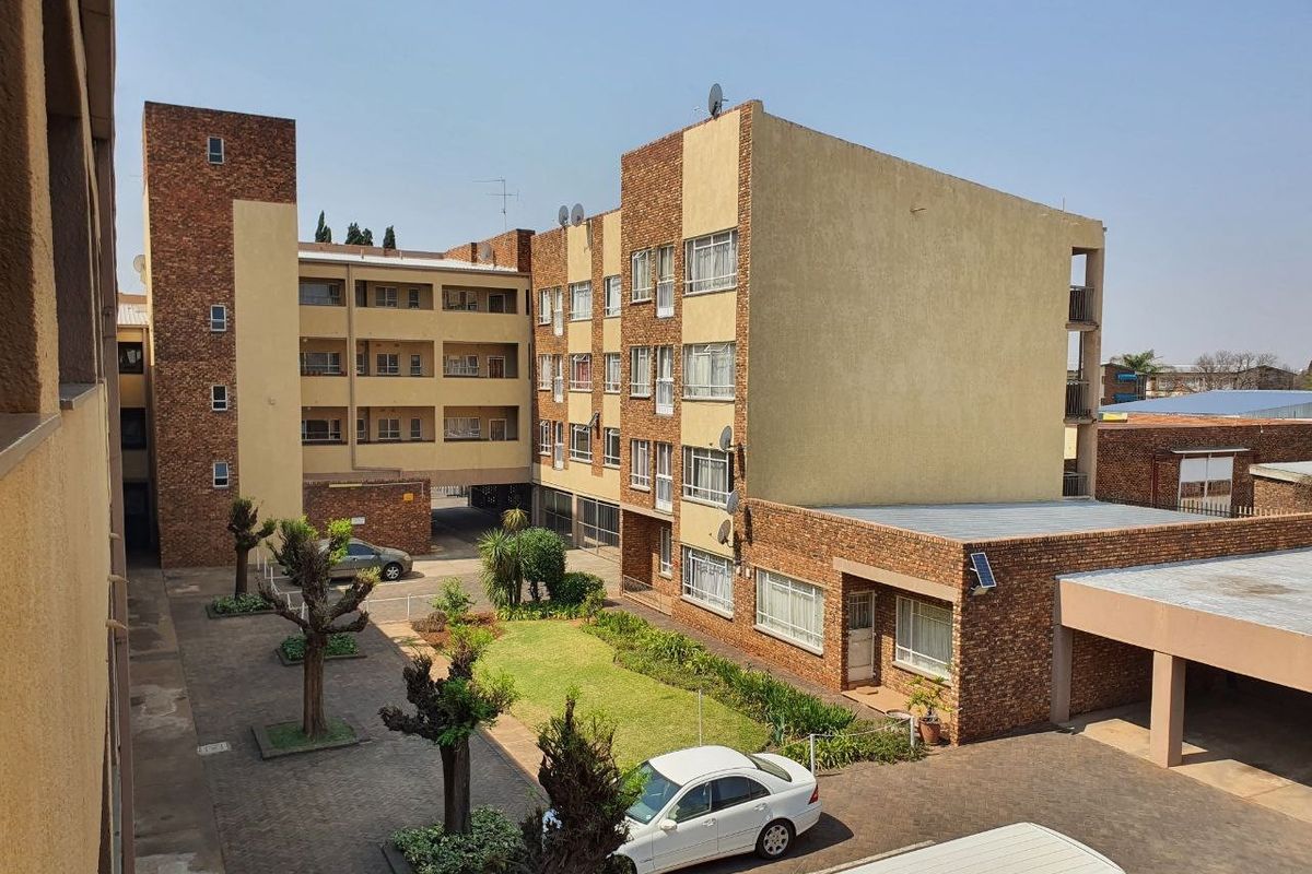 An elevated view of the apartment complex exterior, featuring a central paved courtyard, landscaped garden areas, and covered parking facilities.