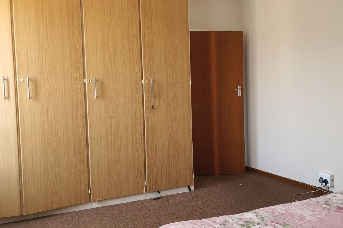 A bedroom featuring built-in wooden cupboards and carpeted flooring, providing functional storage space within the apartment.