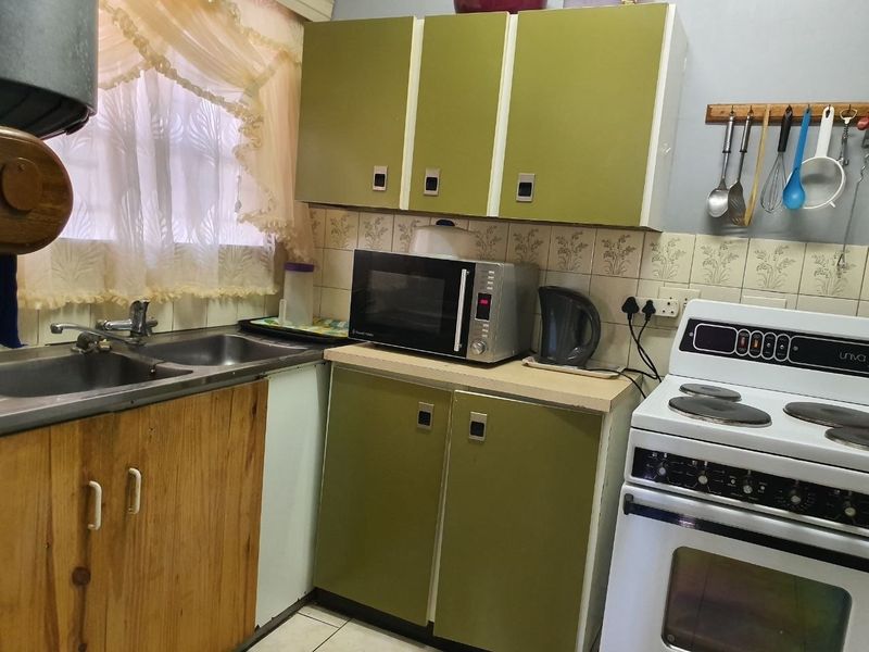 A compact kitchen featuring dated green cabinetry, a double sink, tiled backsplash, and a freestanding stove, offering potential for a modern renovation.
