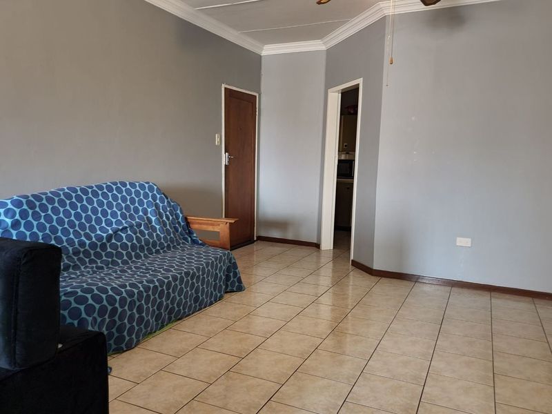 A living room featuring tiled flooring, ceiling cornice, and a ceiling fan, with access to an adjacent room.
