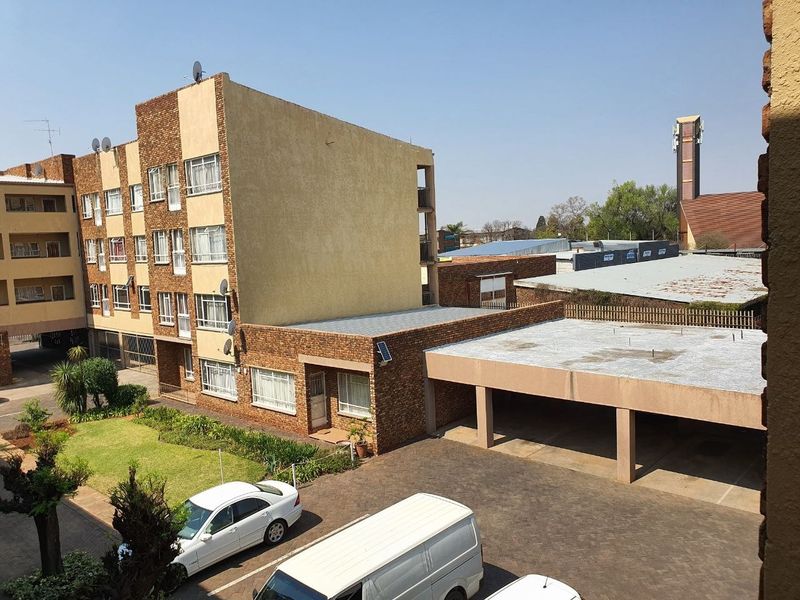 Exterior view of an apartment complex featuring a brick facade, covered parking bays, and a well-maintained communal garden area.