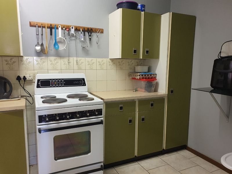 A functional kitchen featuring dated olive green cabinetry, a freestanding electric stove, tiled splashback, and laminate countertops.