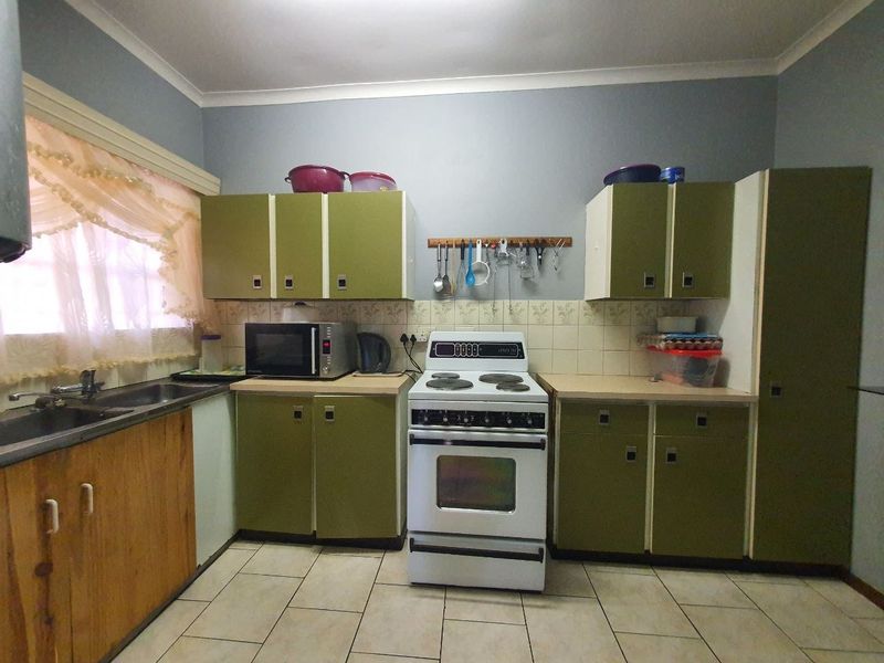 A functional kitchen featuring dated green cabinetry, a freestanding stove, tiled backsplash, and tiled flooring, offering potential for a modern renovation.