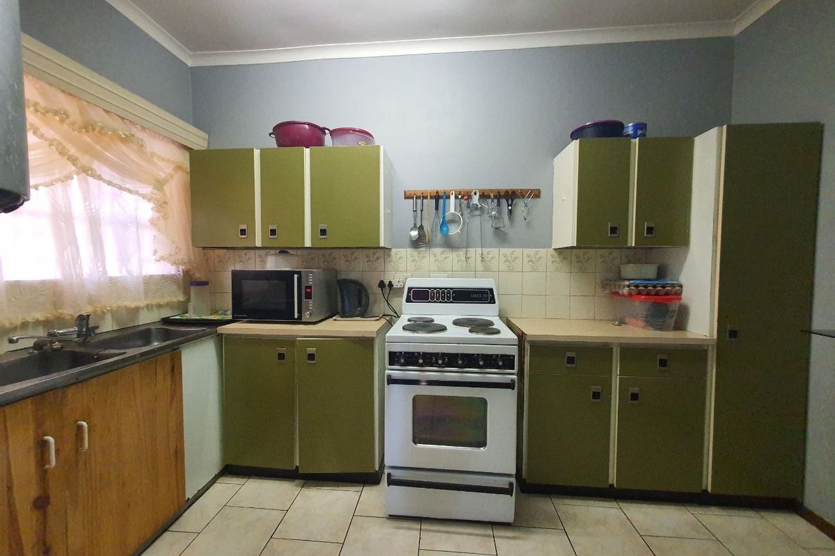 A functional kitchen featuring dated green cabinetry, a freestanding stove, tiled backsplash, and tiled flooring, offering potential for a modern renovation.