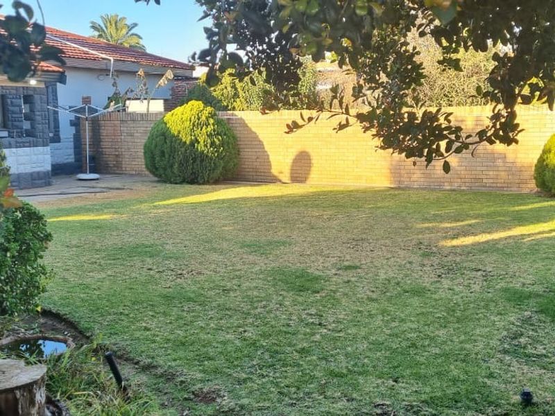 A spacious rear garden featuring a well-maintained lawn, established shrubs, and a solid brick boundary wall providing privacy.