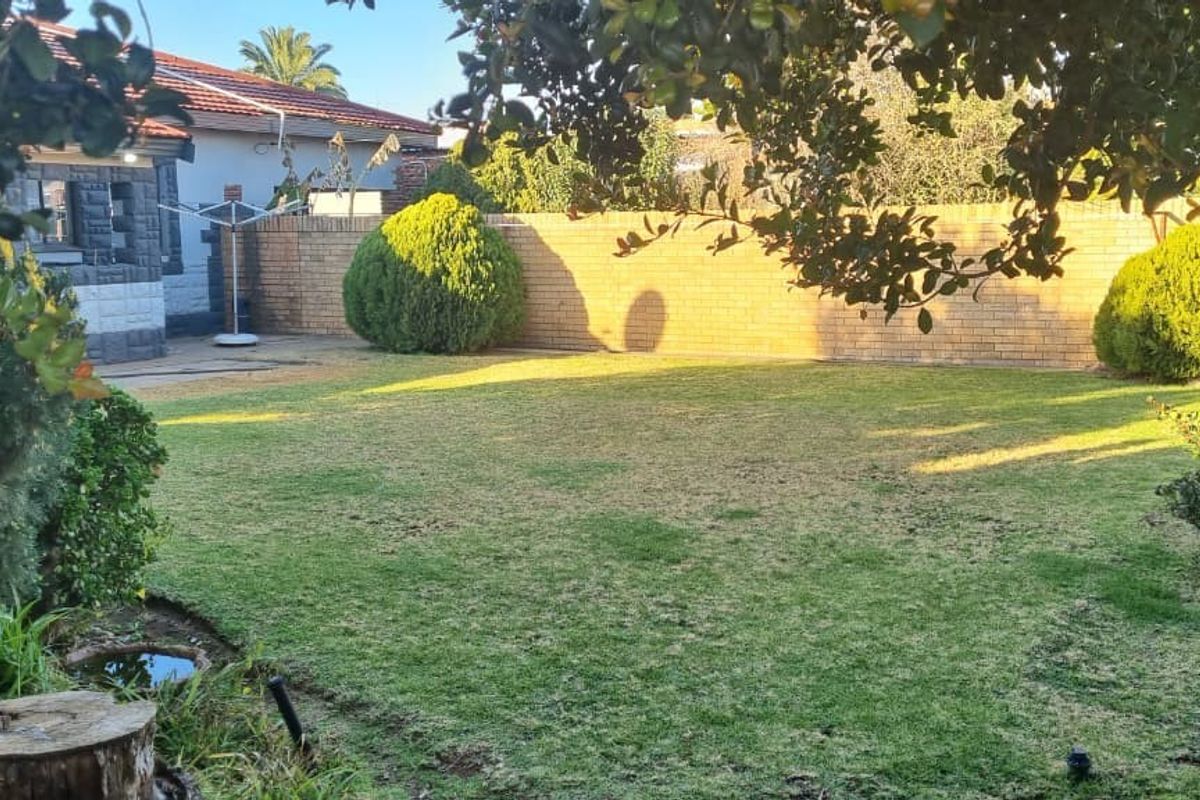 A spacious rear garden featuring a well-maintained lawn, established shrubs, and a solid brick boundary wall providing privacy.