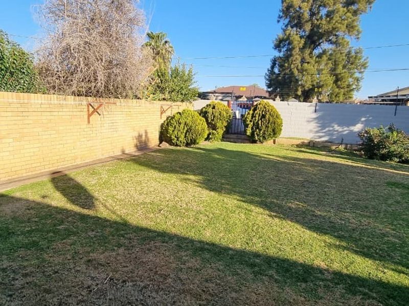 A spacious private backyard featuring a lawn area enclosed by brick and painted masonry boundary walls with established perimeter shrubbery.