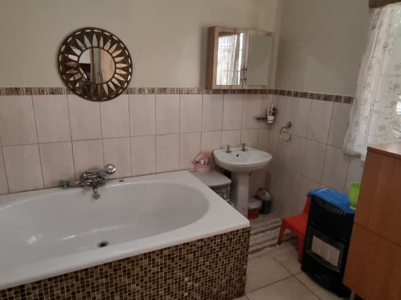 A functional bathroom featuring a built-in bathtub with mosaic tiling and a pedestal basin, offering a dated but practical layout.