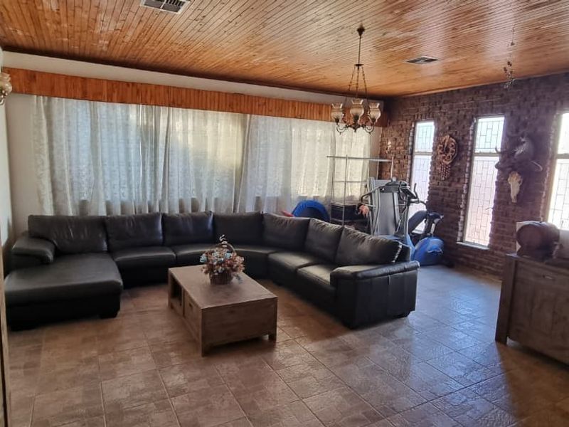 Spacious living room featuring a timber-clad ceiling, exposed brick feature wall, and tiled flooring, offering a rustic aesthetic with ample natural light.