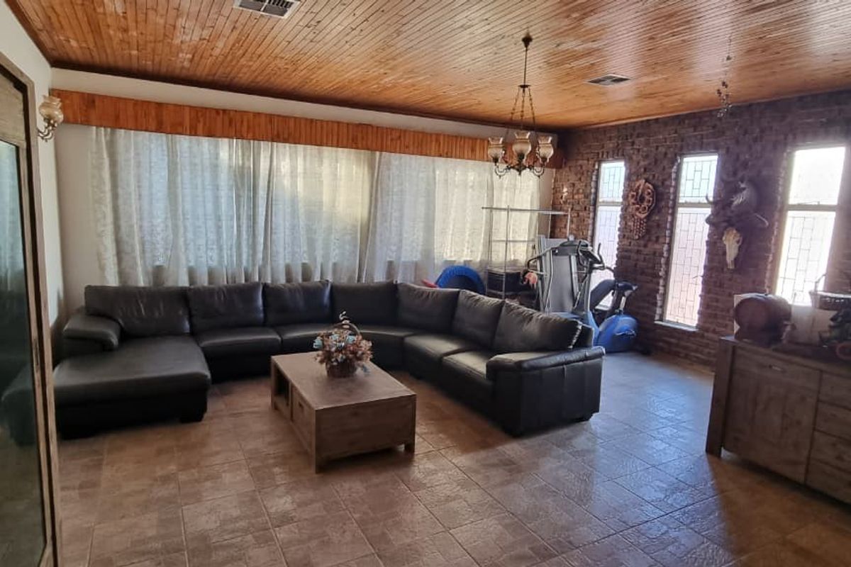 Spacious living room featuring a timber-clad ceiling, exposed brick feature wall, and tiled flooring, offering a rustic aesthetic with ample natural light.