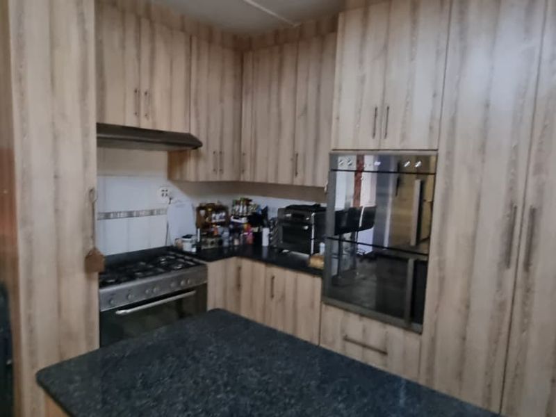 A functional kitchen featuring wood-look cabinetry, granite countertops, a gas hob, extractor fan, and a built-in oven, with an adjacent breakfast bar area.