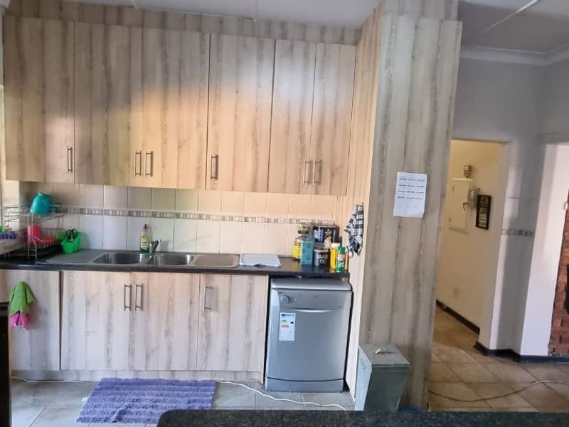 A functional kitchen featuring light wood-look cabinetry, a double bowl sink, tiled backsplash, and an adjacent exposed brick wall feature.
