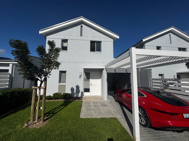Modern townhouse front elevation featuring a paved driveway with a pergola, stone entrance path, and well-maintained front lawn.