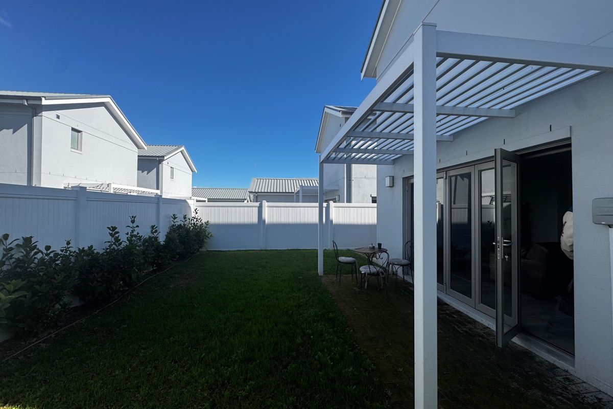 Rear exterior view of the townhouse featuring a private lawn, white vinyl fencing, and a covered patio area with bi-fold doors.