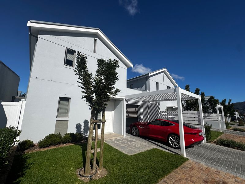 Modern townhouse exterior featuring a clean facade, paved driveway, and a white pergola structure, set within a well-maintained residential environment.