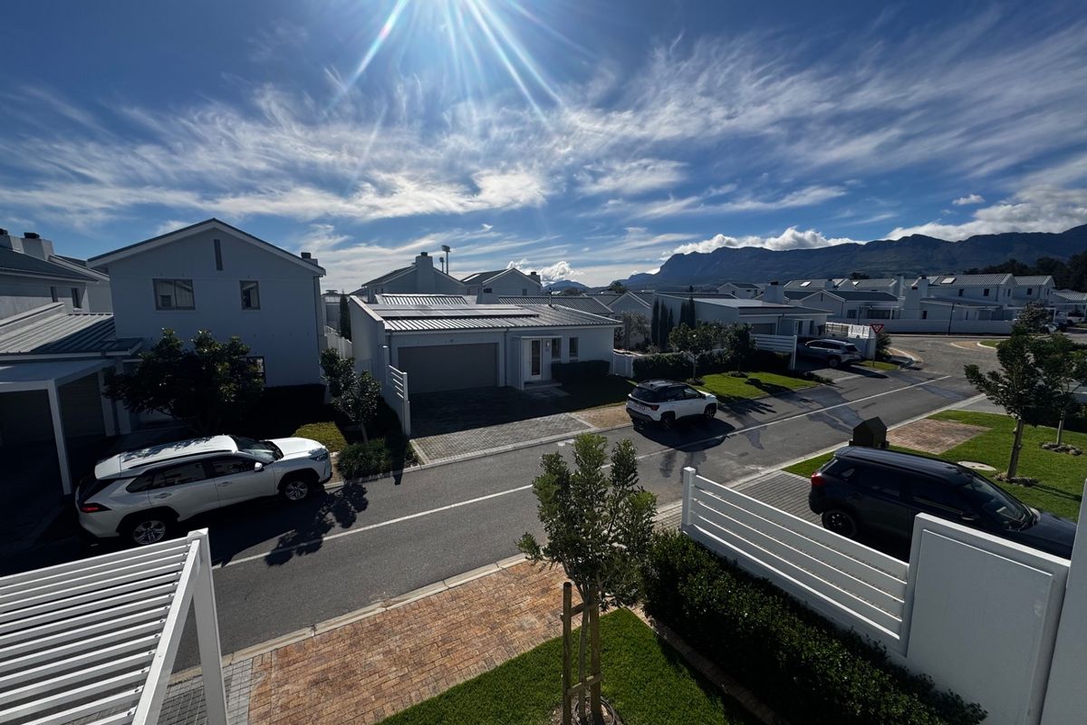 An elevated aerial view of a modern townhouse complex featuring paved driveways, garages, and well-maintained landscaped gardens under a clear blue sky.