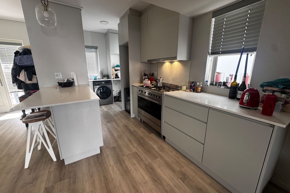 Modern kitchen featuring sleek cabinetry, stone countertops, a gas stove with extractor, and a functional island, seamlessly connected to a laundry area.