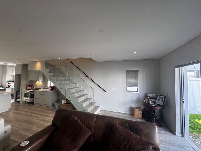 Open-plan living area featuring modern laminate flooring, a contemporary staircase with glass balustrade, and a sleek kitchen with integrated stainless steel appliances.