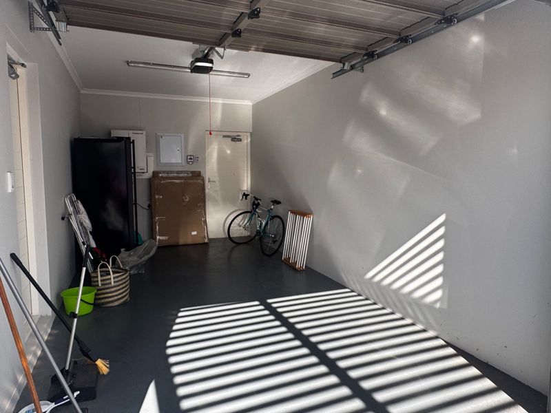 A clean and well-maintained single garage featuring a sectional door, painted concrete flooring, and integrated electrical distribution board.