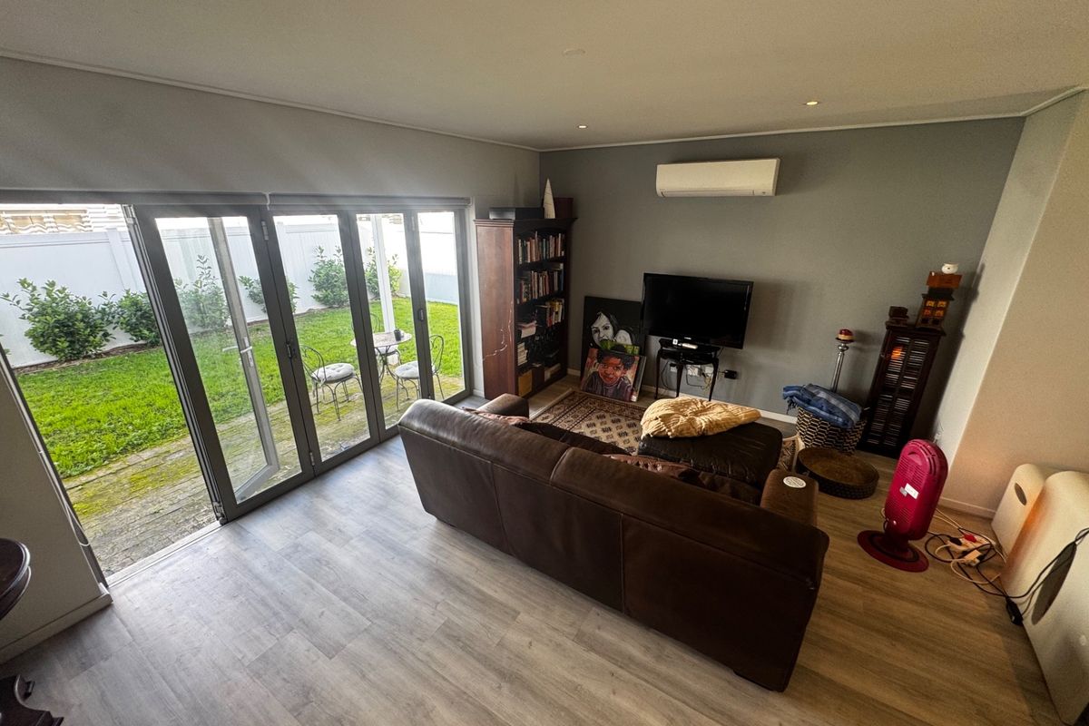 Spacious living room featuring modern laminate flooring, recessed downlights, a split-system air conditioner, and large bi-fold doors opening to a private garden.