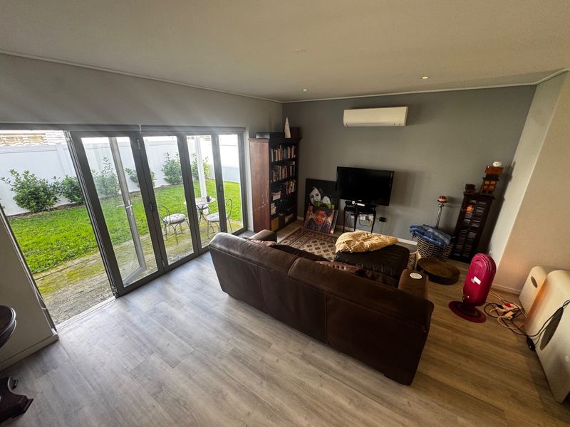 Spacious living room featuring modern laminate flooring, recessed downlights, a split-system air conditioner, and large bi-fold doors opening to a private garden.