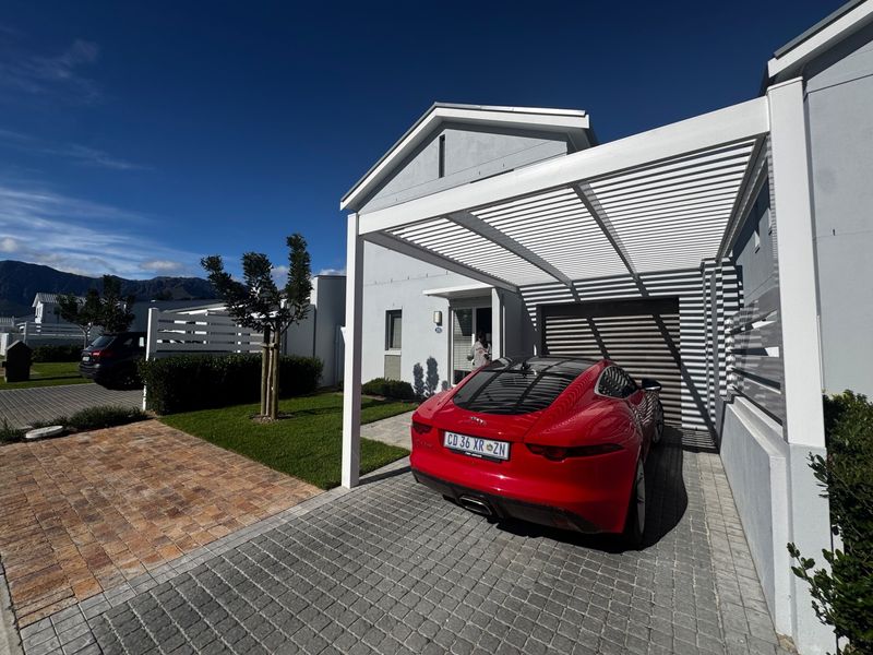 Front exterior view of the townhouse featuring a modern white pergola, paved driveway, and well-maintained garden area.