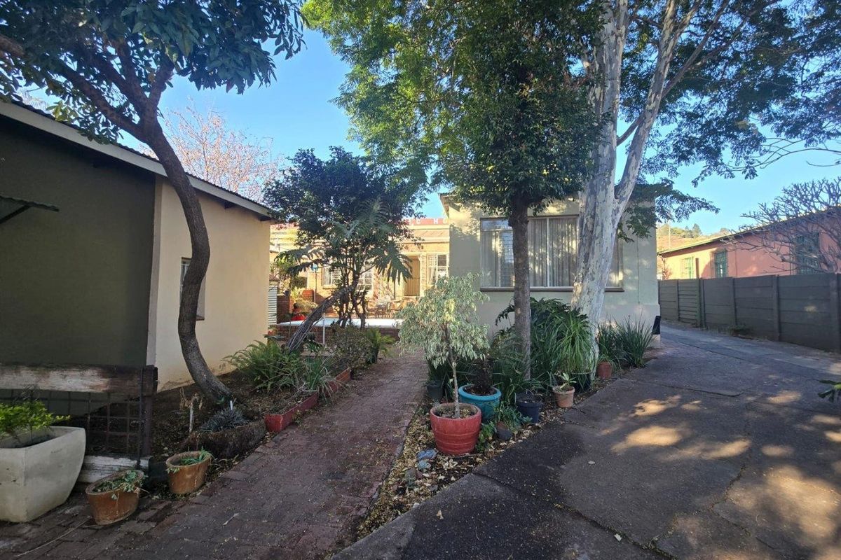 A rear garden area featuring a brick paved pathway, concrete driveway, and established trees, providing access to the rear elevation of the house.