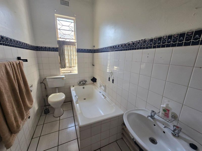 A dated bathroom featuring a standard bathtub, pedestal basin, and toilet with original tiled finishes, requiring modernization and cosmetic updates.