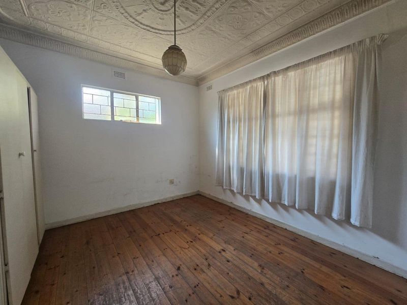 A vacant bedroom featuring original pressed metal ceilings, timber flooring, and a built-in wardrobe, offering a blank canvas for renovation.