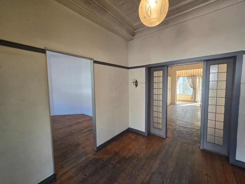 An empty living area featuring original timber flooring, decorative plaster ceilings, and classic sliding glass doors connecting to adjacent rooms.