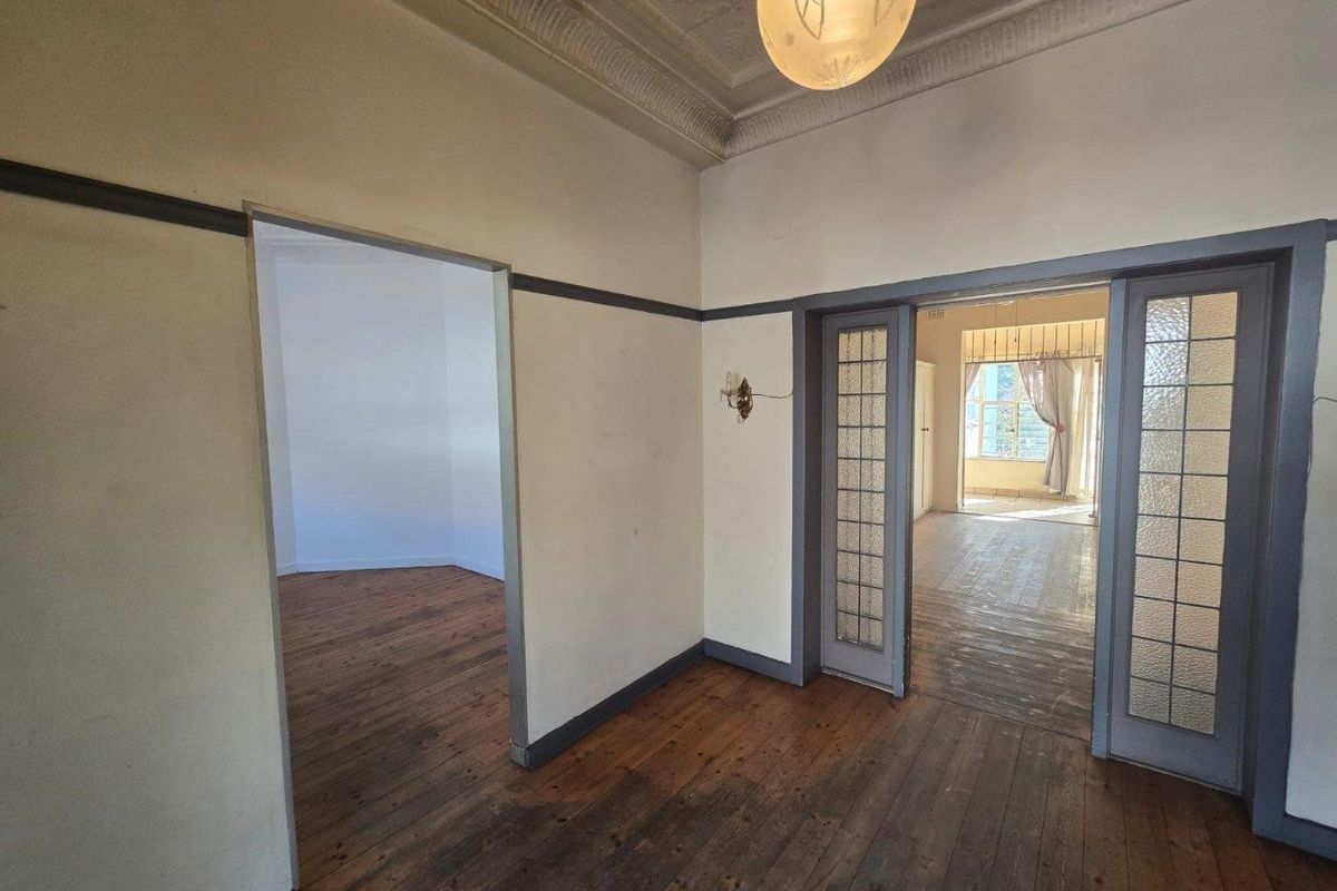 An empty living area featuring original timber flooring, decorative plaster ceilings, and classic sliding glass doors connecting to adjacent rooms.