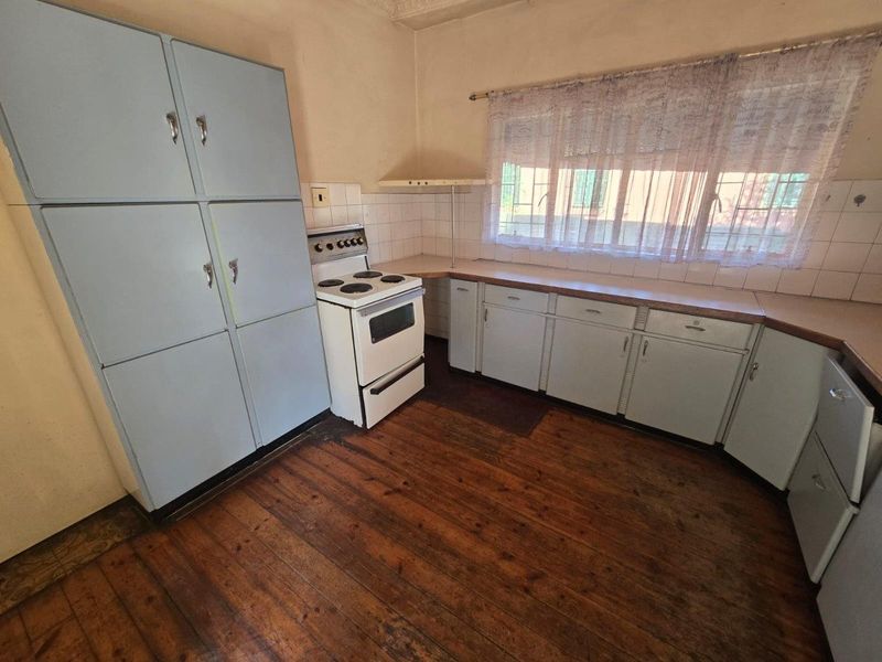 A dated kitchen featuring original timber flooring, built-in cabinetry, and a freestanding stove, offering significant potential for a modern renovation.