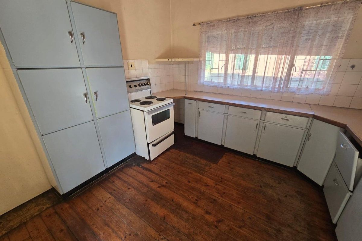 A dated kitchen featuring original timber flooring, built-in cabinetry, and a freestanding stove, offering significant potential for a modern renovation.