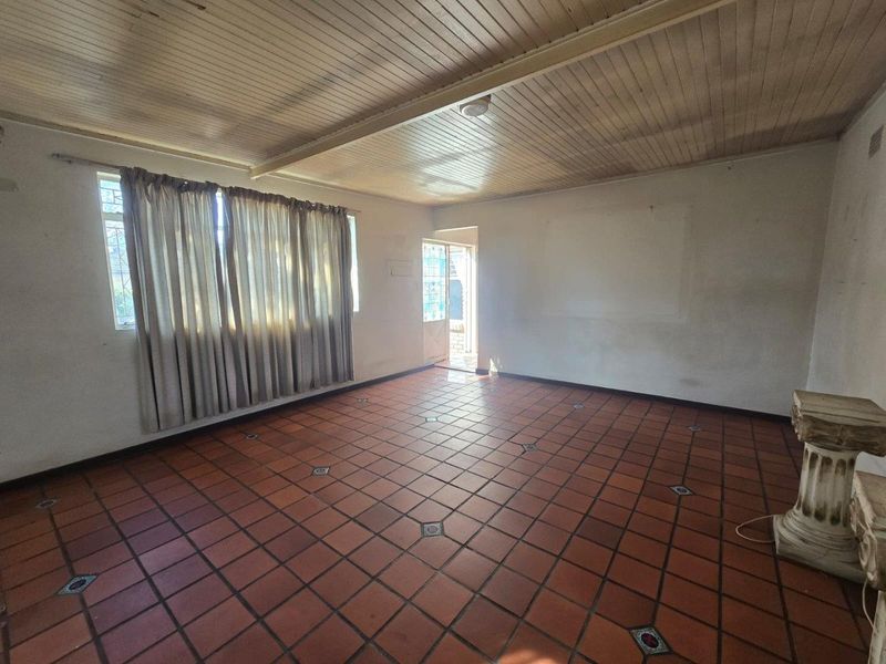 An empty living room featuring terracotta tile flooring and a timber tongue and groove ceiling, offering a blank canvas for renovation.