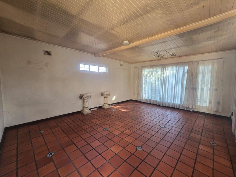 Spacious living area featuring terracotta tile flooring and a timber panelled ceiling, currently vacant and requiring cosmetic renovation to address ceiling and wall damage.