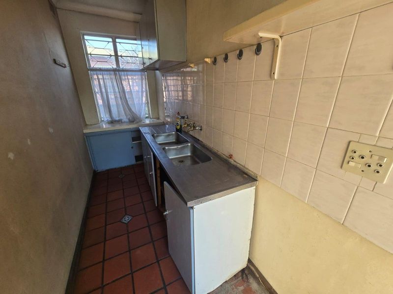 A functional scullery or utility area featuring a double stainless steel sink, tiled splashback, and terracotta flooring, requiring cosmetic updates and repairs.
