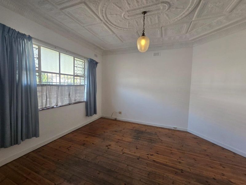 An empty bedroom featuring original timber floorboards, an ornate plaster ceiling, and large casement windows providing natural light.