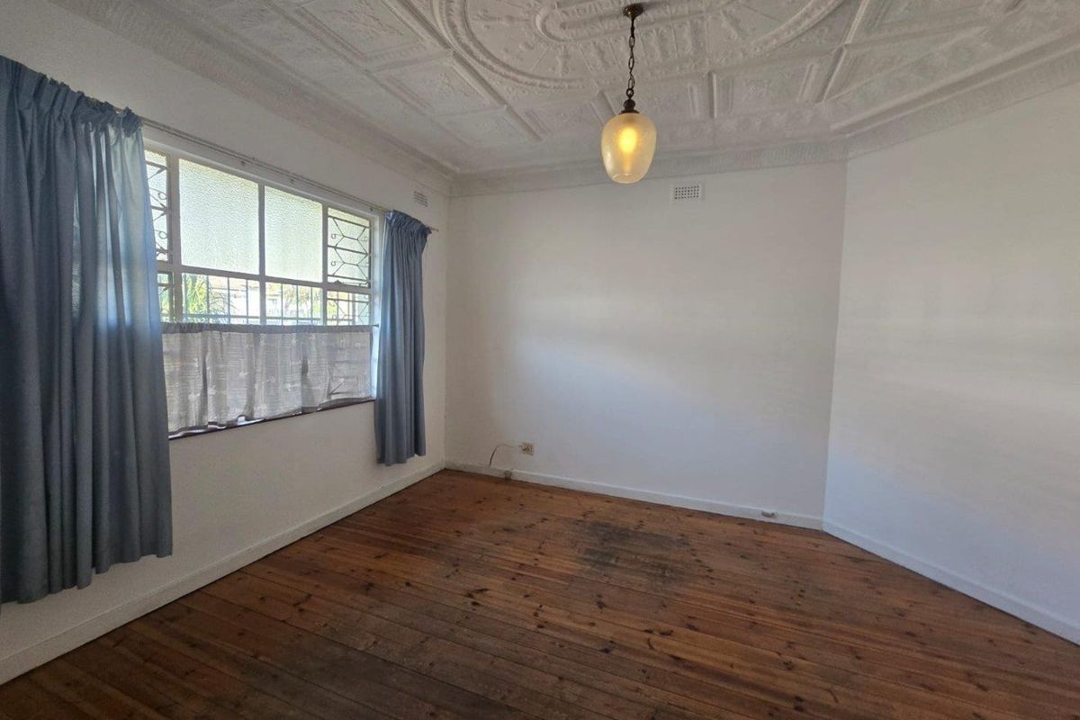 An empty bedroom featuring original timber floorboards, an ornate plaster ceiling, and large casement windows providing natural light.