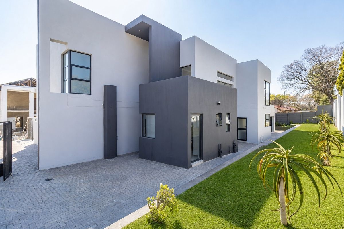 A modern rear exterior view of the property featuring clean architectural lines, a paved driveway, and a well-maintained lawn.