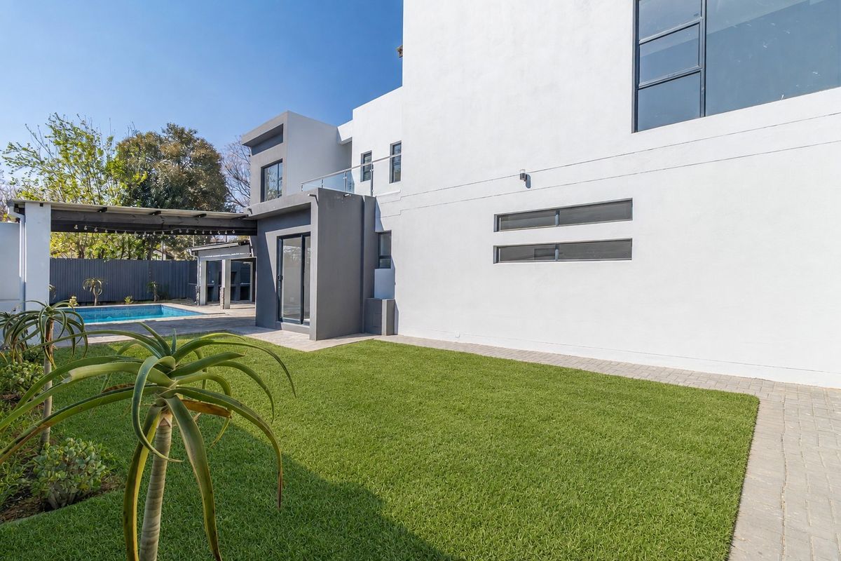 Rear view of a modern two-story home featuring a swimming pool, covered patio area, and well-maintained lawn with paved pathways.