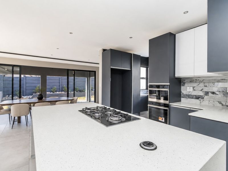 Modern open-plan kitchen featuring a large island with gas hob, built-in appliances, stone countertops, and seamless flow to the outdoor patio area.
