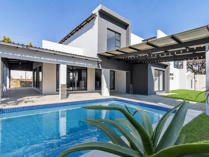 Modern rear exterior featuring a sparkling swimming pool, expansive paved patio area, and covered outdoor entertainment space with contemporary architectural finishes.