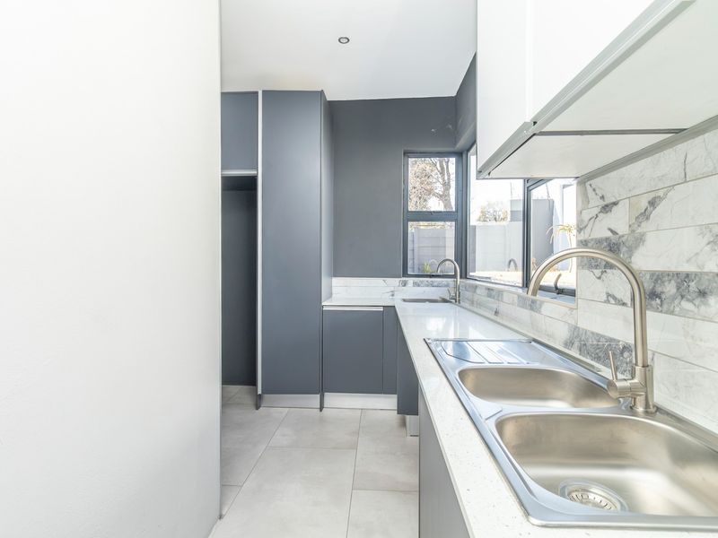 Modern kitchen featuring sleek dark cabinetry, quartz countertops, marble-look tile backsplash, and a double bowl stainless steel sink with a contemporary mixer tap.