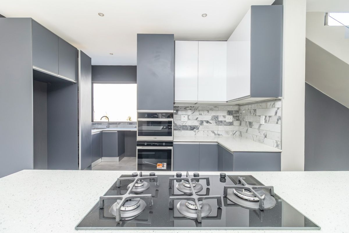 Modern kitchen featuring sleek grey and white cabinetry, stone countertops, a built-in oven, microwave, and a gas hob on the central island.